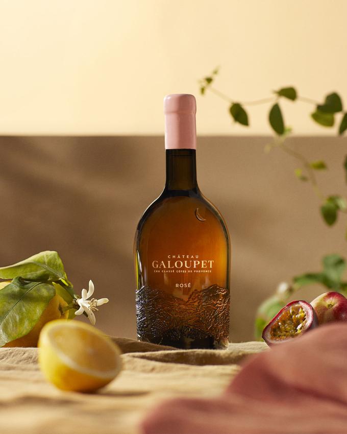 A bottle of Château Galoupet Cru Classé 2023 Rosé inbetween tasting notes, fruits and flowers in late afternoon. 