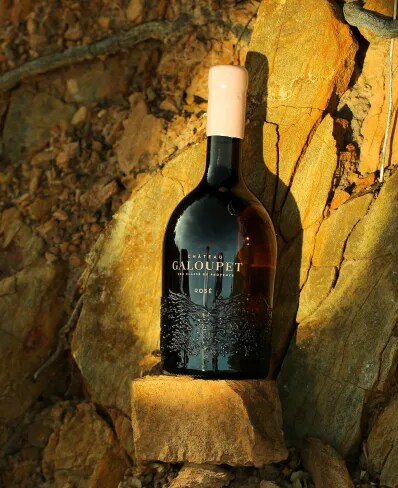 Une bouteille de Château Galoupet Cru Classé Rosé dans la lumière devant la pierre unique du Château