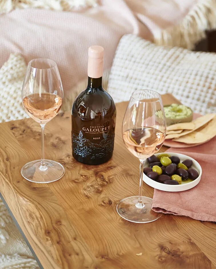 Château Galoupet Cru Classé Côtes de Provence on a wooden table with two served glasses and olives. A couch in the background with cosy cushions